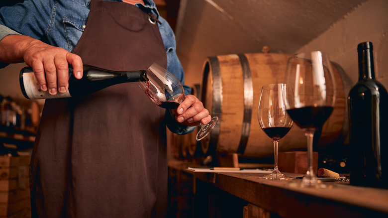 Person in apron pours a glass of red wine