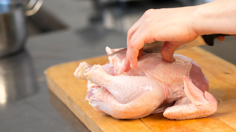 Hands cutting uncooked chicken