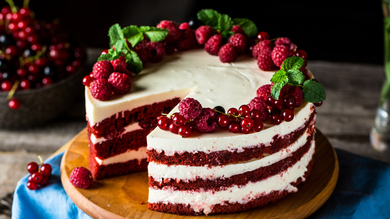 Layered red cake with white frosting, topped with berries and mint