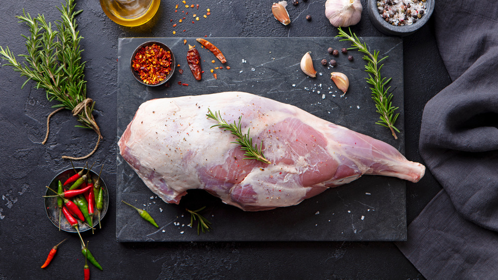 leg of lamb on stone with red and green chilies, garlic, and rosemary