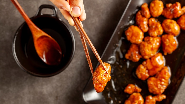 A hand with chopsticks holding Mandarin orange chicken