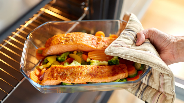 Pink salmon in a clear baking dish being removed from the oven