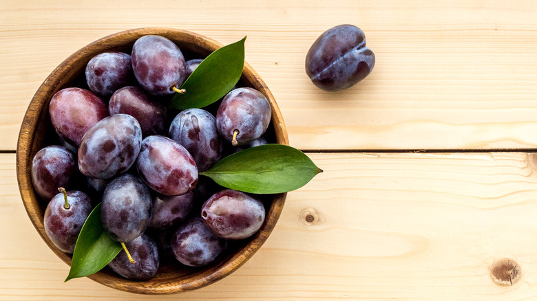 Bowl of plums on wood