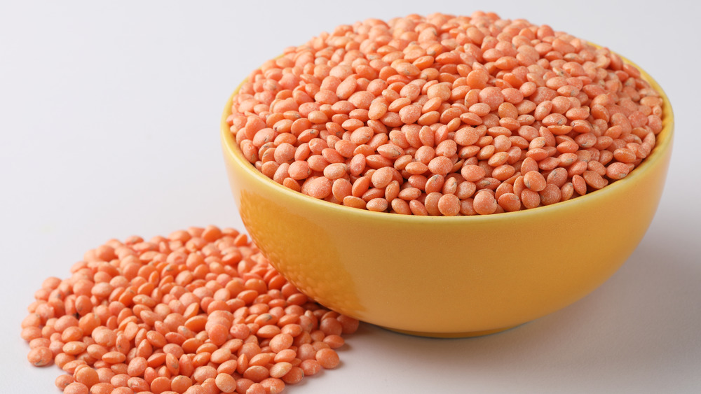 A yellow bowl of dried red lentils against a white background.