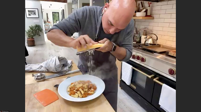 Michael Symon grating cheese over dish