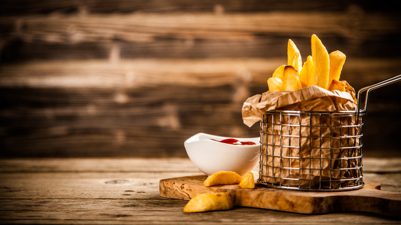 A basket of thick-cut french fries with ketchup on a wooden table and background