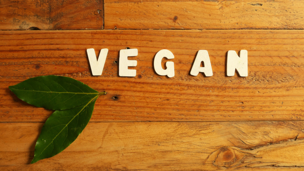 The word vegan spelled with words on wooden surface with leaves nearby