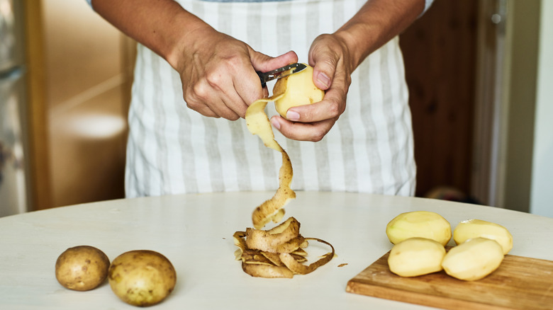 Hands peeling potatoes to slice