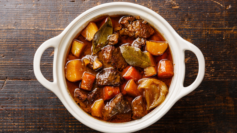 White bowl of beef stew with veggies on wooden table