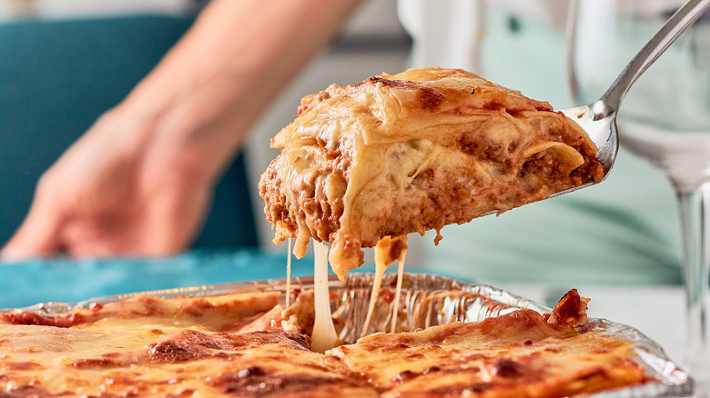 Someone serving up a portion of lasagna from a big platter