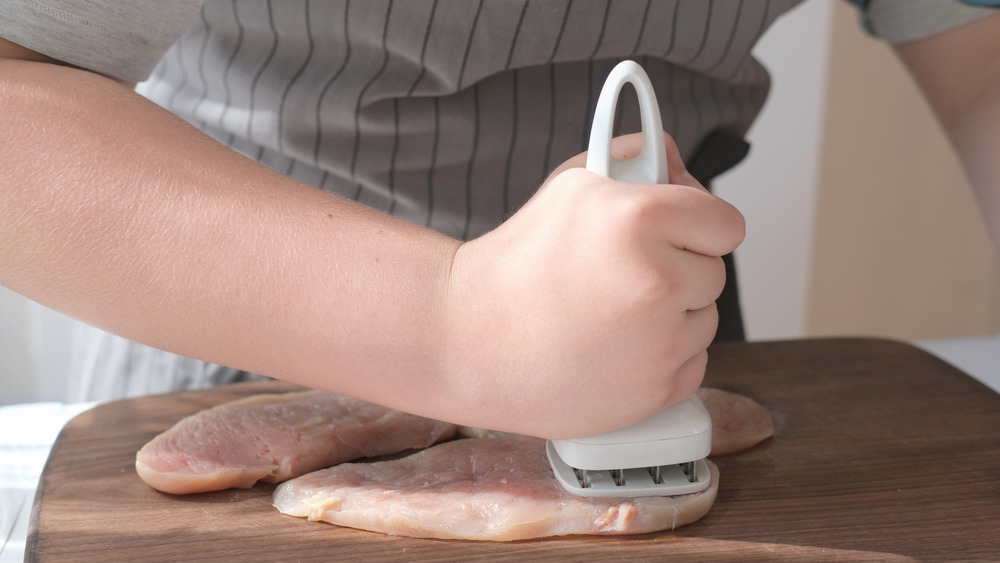 Hand using a tenderizer to flatten out pieces of chicken