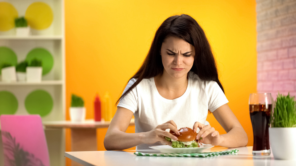 Woman eating burger and looking upset