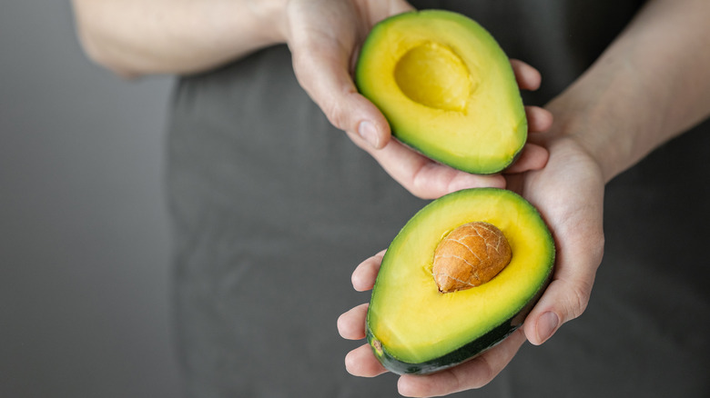 hands holding halved avocado