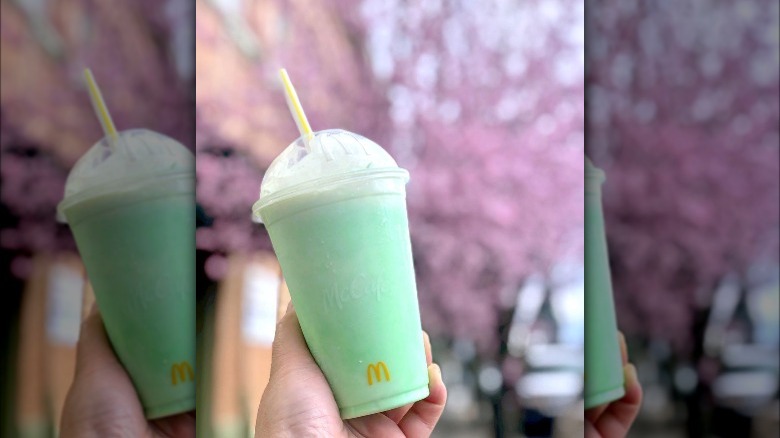 McDonald's Shamrock Shake held in front of cherry blossom tree