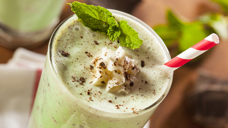 A green shake with whipped cream, mint leaves and a straw