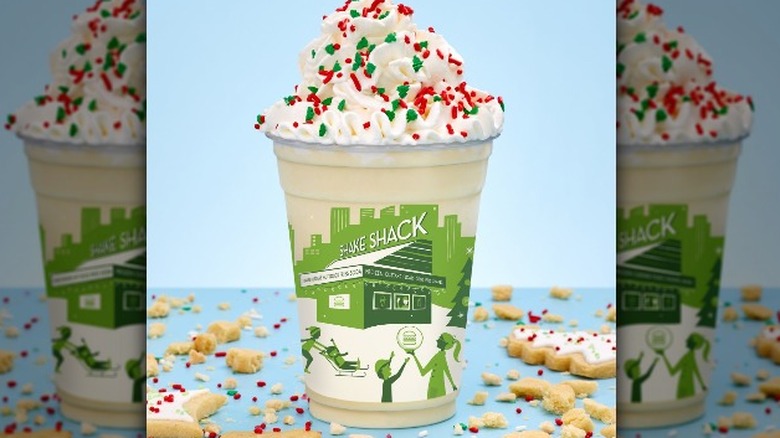 Shake Shack's Christmas Cookie Shake topped with whipped cream and red and green sprinkles. cookie pieces around cup