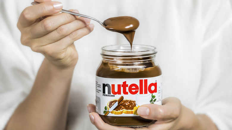 Woman holding spoonful of Nutella over jar