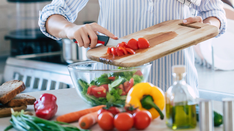 A person scraping chopped tomatoes off a cutting board into a bowl.