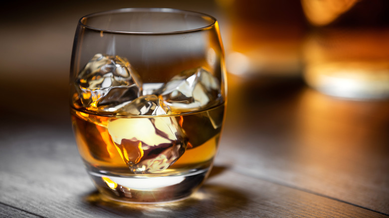 A glass of bourbon over ice, on a wooden surface