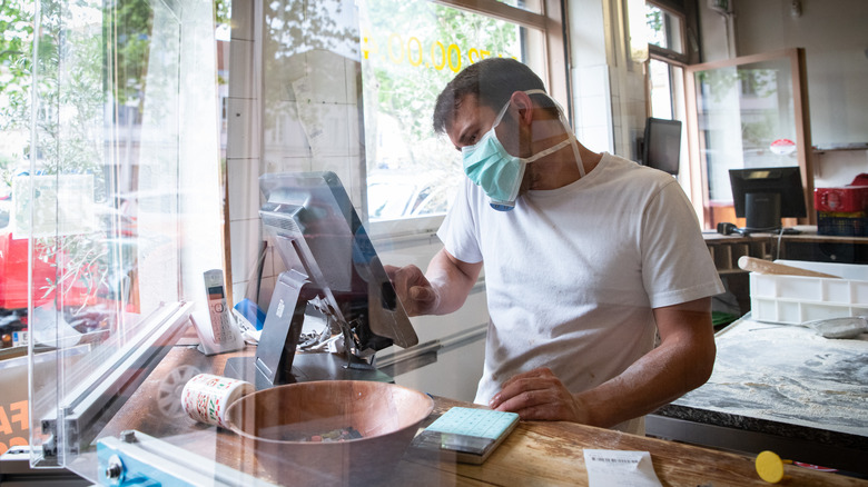 Man with mask on taking orders at pizza shop