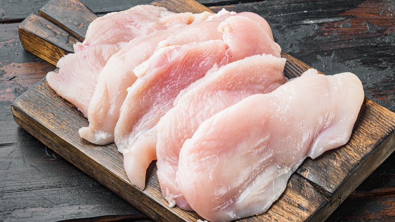 Chicken breasts slice thin on dark board