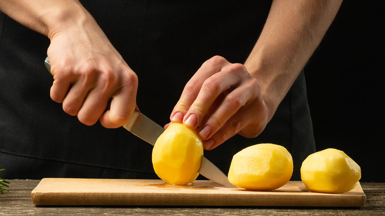 Hands slicing peeled potatoes with a knife