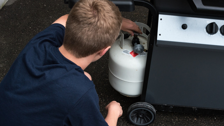 Person turning the valve on a propane tank attached to a gas grill