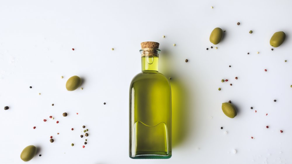 olive oil surrounded by olives against a white background