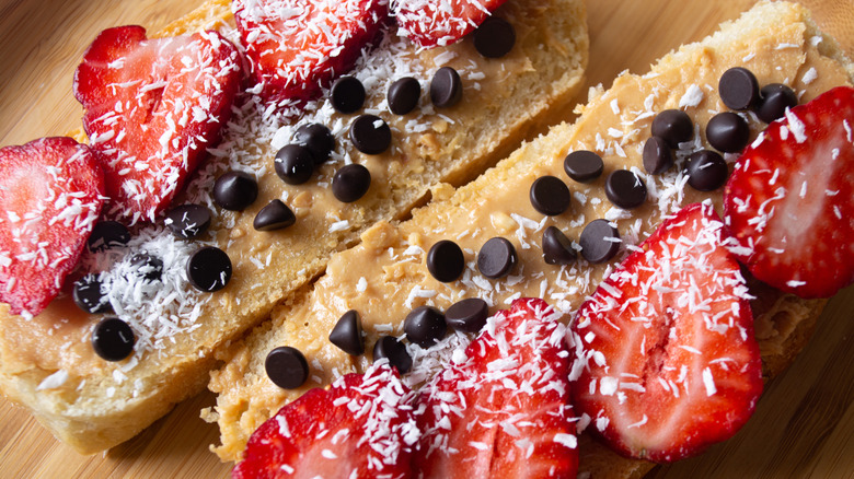 Peanut butter, strawberries, chocolate chips, and coconut shreds spread over two slices of bread