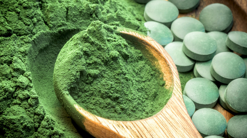 Spirulina powder in a spoon and tablets