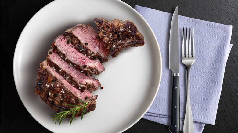 Sliced ribeye on white plate with knife and fork