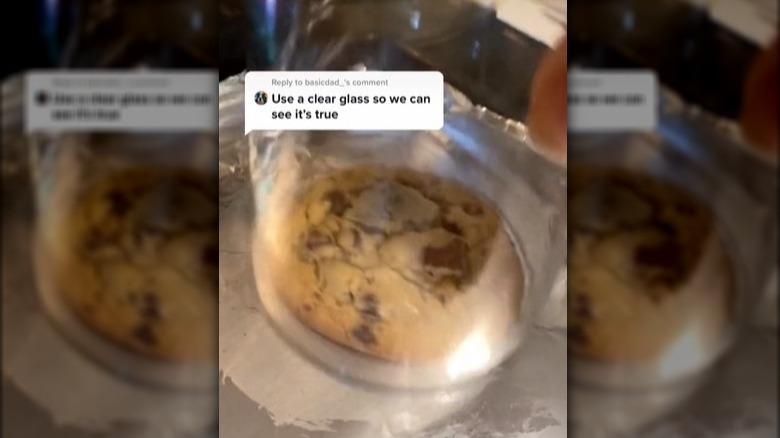 A fresh-baked chocolate chip cookie with a glass over it