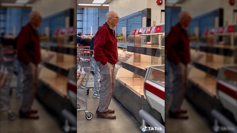 A Costco shopper watching a deli employee take fresh rotisserie chickens out of the oven.