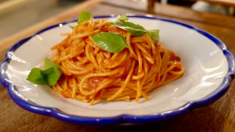 spaghetti with marinara sauce with oil being drizzled on and garnished with basil