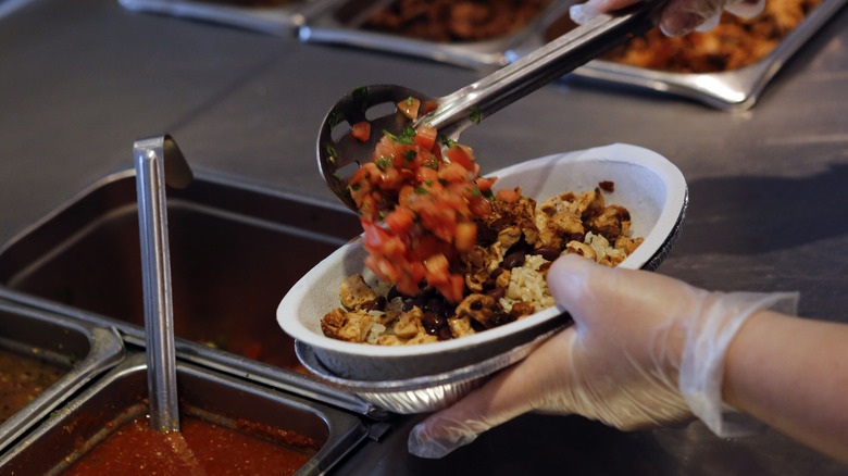 Chipotle employee scooping pico de gallo onto a burrito bowl