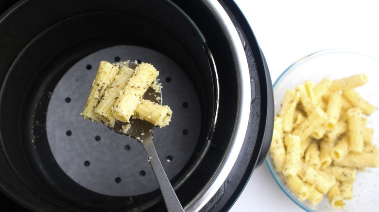 A spoon putting pasta into an air fryer