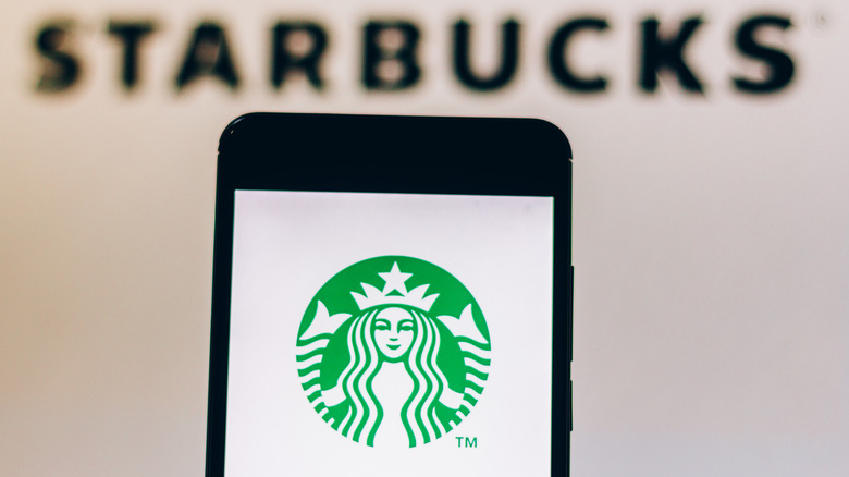 The Starbucks logo is seen on a smartphone screen in front of a Starbucks 