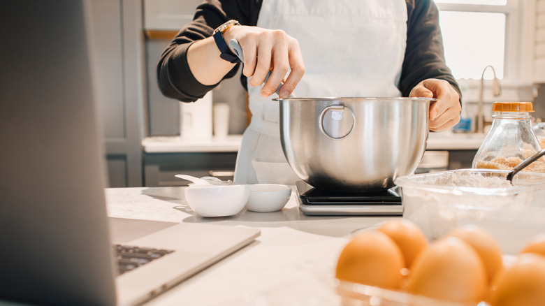 Person mixing bowl on kitchen scale at counter with baking ingredients