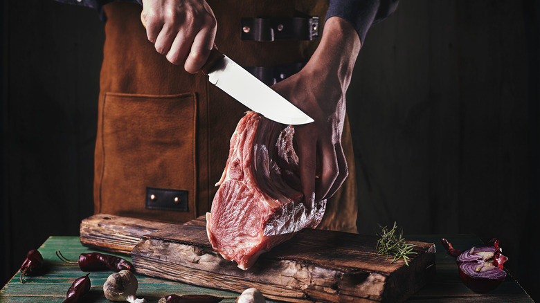 Man in apron cutting large piece of raw meat