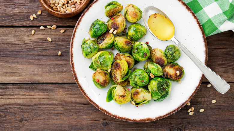 plate of roasted brussels sprouts with spoonful of butter sauce and roasted pine nuts on wooden table