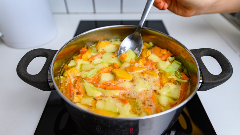 hand putting spoon into pot of simmering vegetables on stovetop