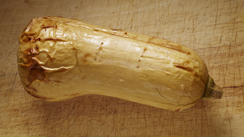 intact whole roasted butternut squash on scarred wooden surface