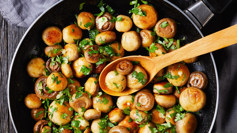 wooden spoon in nonstick skillet full of golden brown button mushrooms with fresh parsley