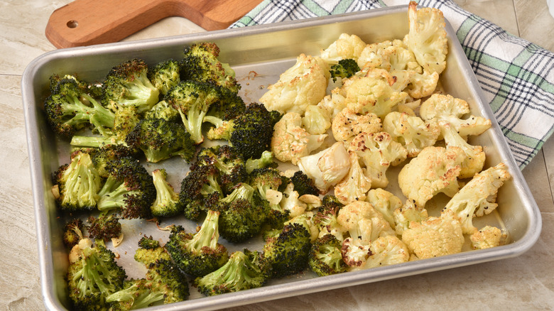 sheet pan of roasted broccoli and cauliflower sitting on plaid kitchen towel