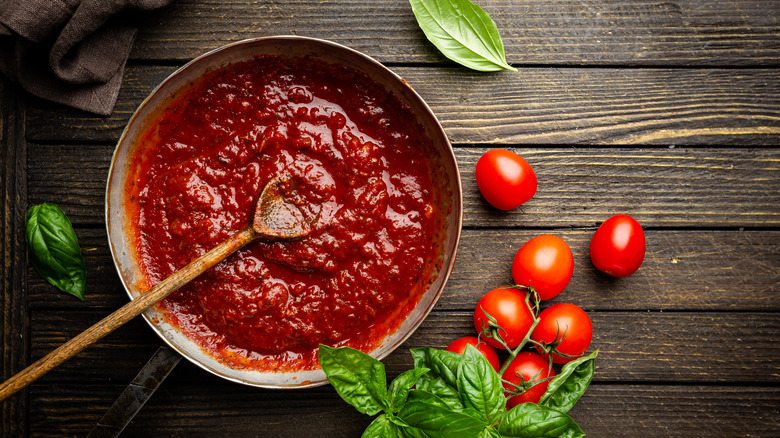 pan of homemade tomato sauce on wooden table with fresh basil and raw tomatoes alongside