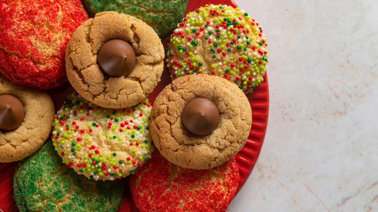 red plate of peanut butter blossoms and round sugar cookies rolled in Christmas colored sprinkles and red and green sugar