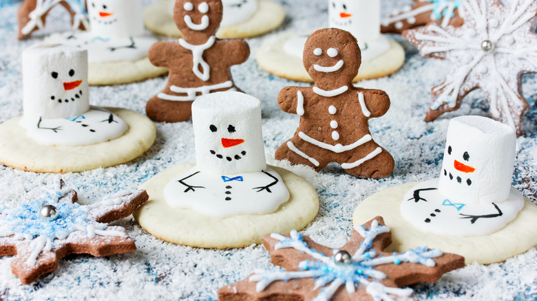 assortment of gingerbread men, gingerbread snowflakes, and melting snowmen cookies with marshmallows all arranged on a surface covered in powdered sugar