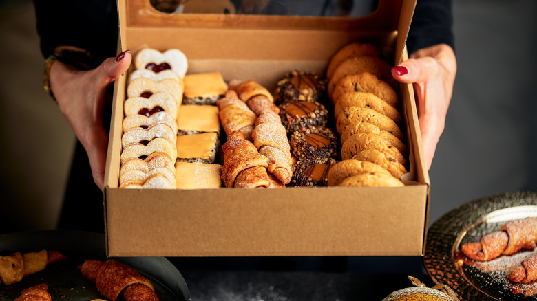 woman's hands holding cardboard bakery box filled with assorted cookies to illustrate cookie exchange concept