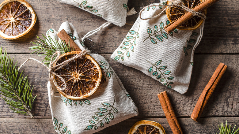 small fabric bags tied with twine with dried orange slices, cinnamon sticks, and pine sprigs on wooden table