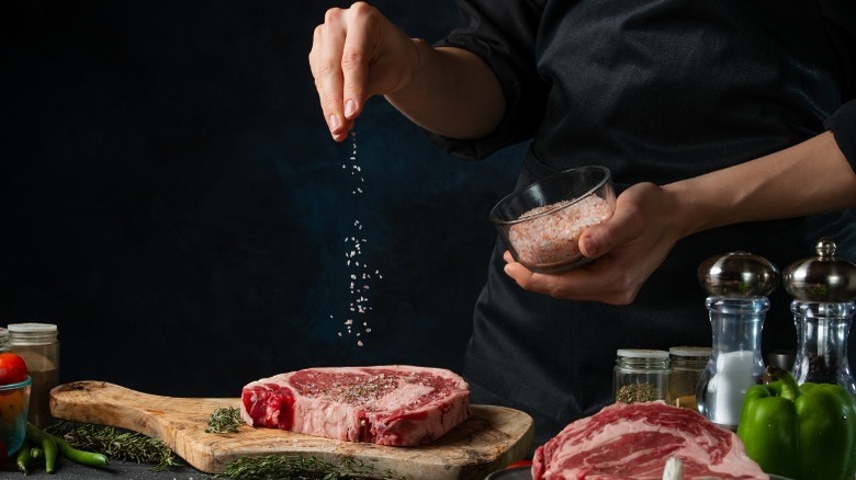 person sprinkling salt over raw steak